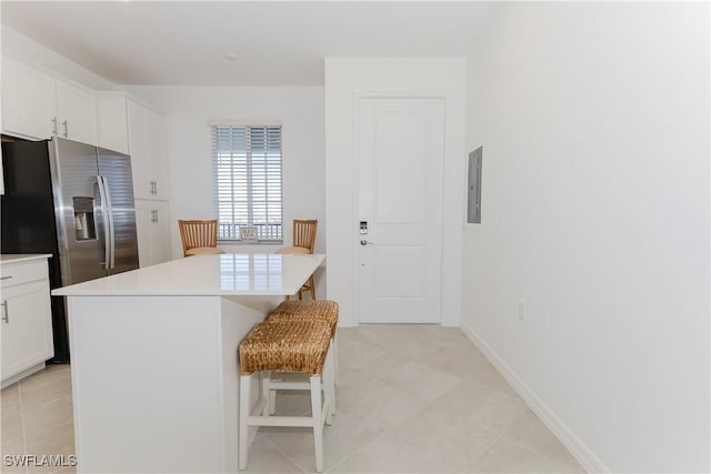 kitchen with a center island, white cabinetry, stainless steel fridge with ice dispenser, a breakfast bar, and electric panel