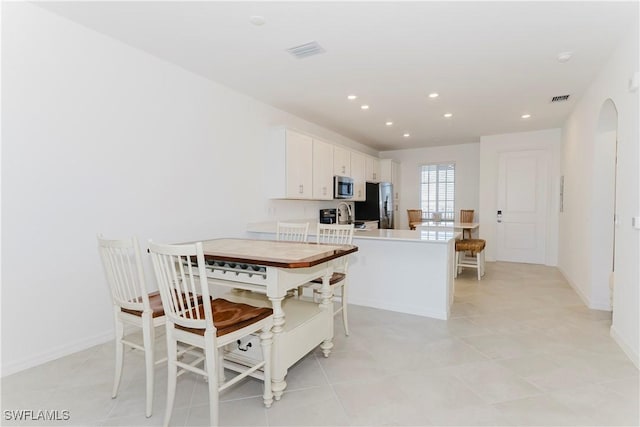 kitchen with kitchen peninsula, sink, white cabinetry, appliances with stainless steel finishes, and light tile patterned floors