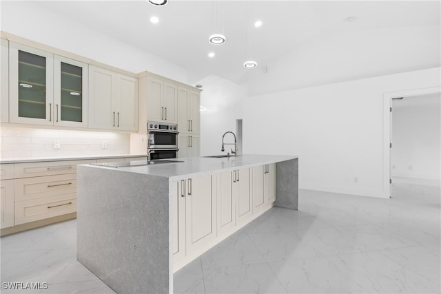 kitchen featuring a center island with sink, sink, decorative backsplash, and double oven