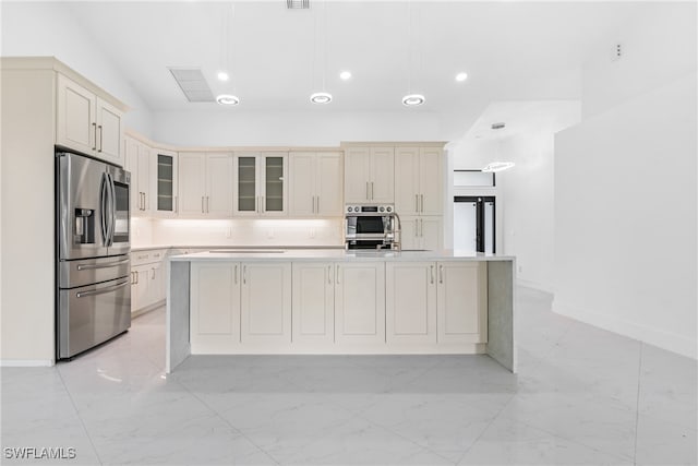 kitchen with hanging light fixtures, cream cabinets, backsplash, appliances with stainless steel finishes, and a center island with sink