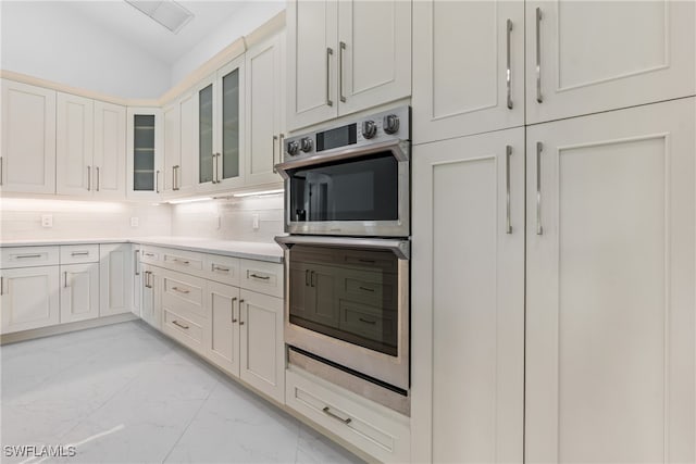 kitchen featuring lofted ceiling, white cabinets, double oven, and tasteful backsplash