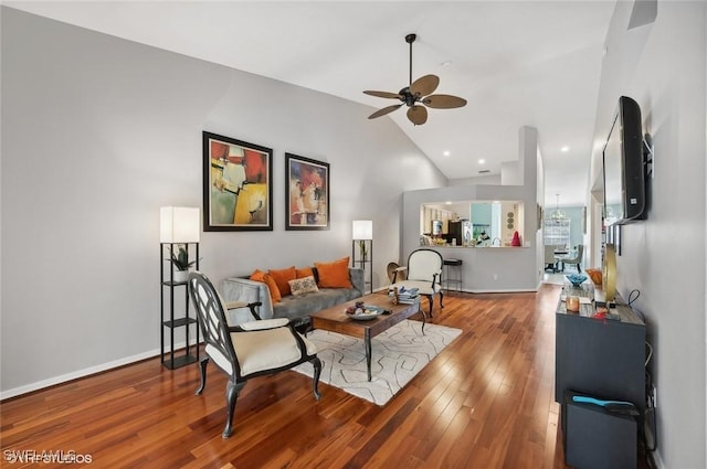 living area with a ceiling fan, high vaulted ceiling, baseboards, and wood finished floors