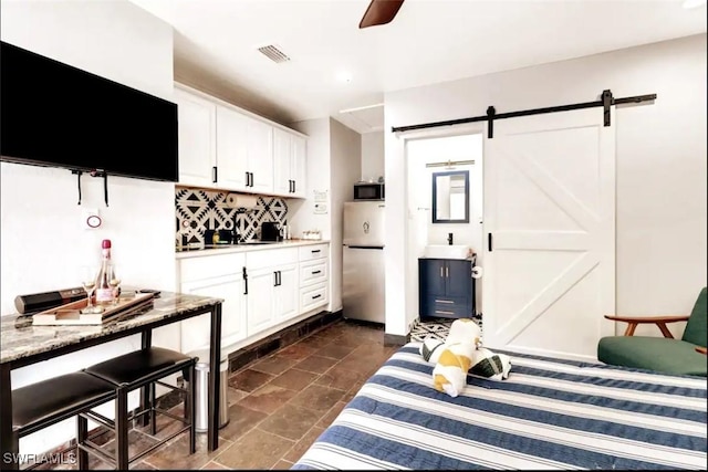 1797 42nd Ter SW, Naples, FL 34116 - bedroom featuring freestanding refrigerator, a barn door, a sink, dark stone finish floors, and a ceiling fan