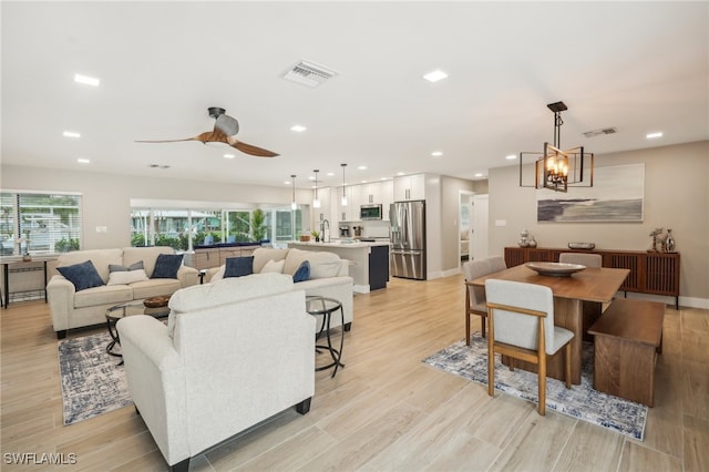 living room featuring light hardwood / wood-style flooring, sink, and ceiling fan with notable chandelier