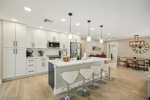 kitchen featuring a kitchen island with sink, white cabinetry, stainless steel appliances, hanging light fixtures, and light hardwood / wood-style floors