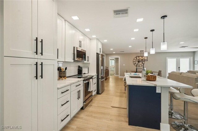 kitchen with light wood-type flooring, stainless steel appliances, light stone countertops, a center island with sink, and white cabinets