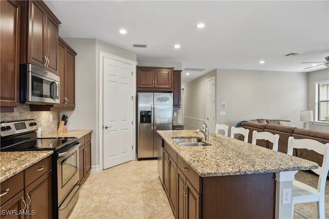 kitchen featuring a kitchen island with sink, stainless steel appliances, a kitchen breakfast bar, sink, and ceiling fan