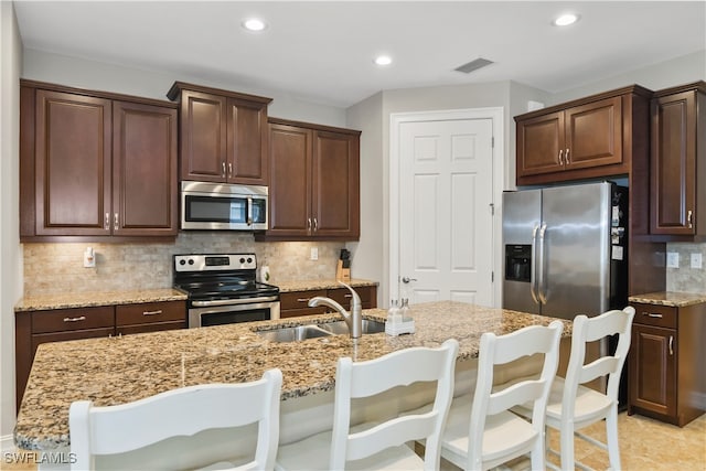 kitchen with light stone countertops, a kitchen island with sink, a kitchen bar, stainless steel appliances, and sink