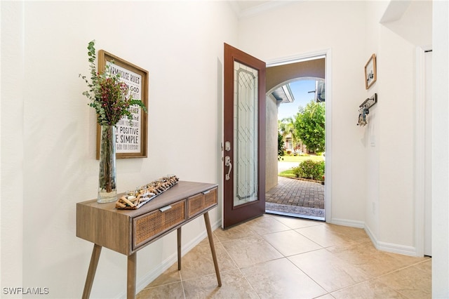 foyer entrance featuring light tile patterned floors, baseboards, arched walkways, and crown molding