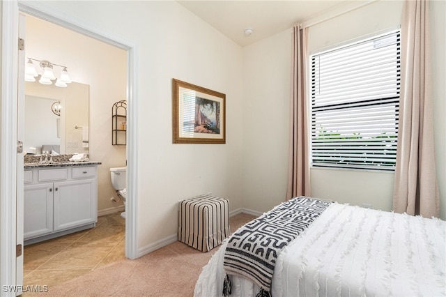 bedroom featuring ensuite bathroom, light tile patterned floors, baseboards, and light colored carpet