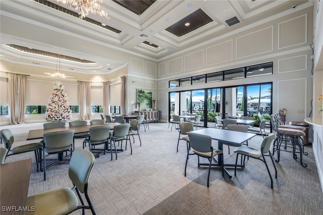 carpeted dining area with crown molding, an inviting chandelier, a towering ceiling, and a decorative wall