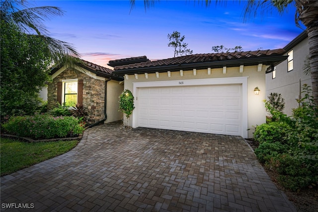 view of front of home featuring a garage, stone siding, a tiled roof, decorative driveway, and stucco siding