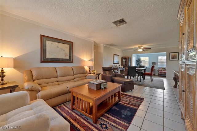 living room featuring ceiling fan, a textured ceiling, crown molding, and light tile patterned floors