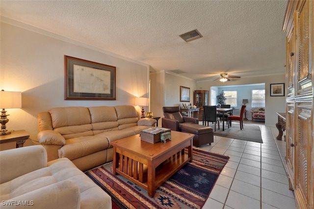 living area featuring light tile patterned floors, visible vents, a textured ceiling, and ornamental molding