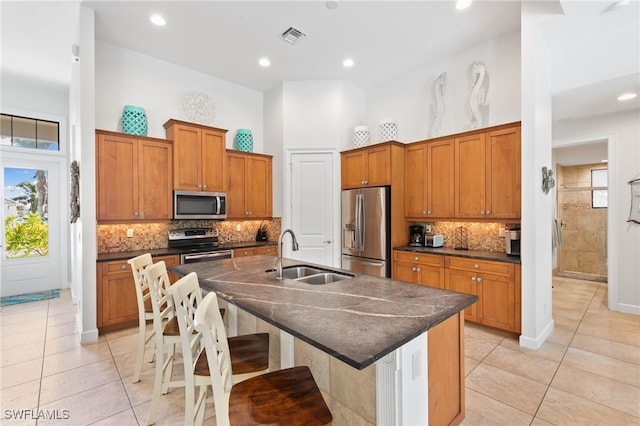 kitchen with a kitchen island with sink, a kitchen bar, stainless steel appliances, sink, and a towering ceiling