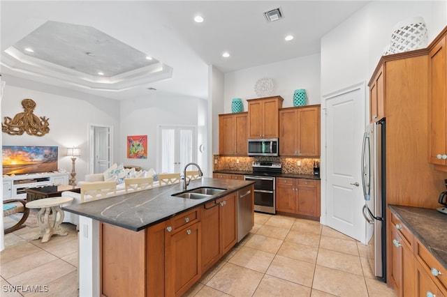 kitchen featuring dark stone counters, stainless steel appliances, an island with sink, sink, and light tile patterned flooring