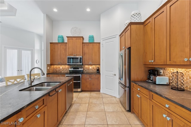 kitchen with dark stone countertops, stainless steel appliances, sink, light tile patterned flooring, and tasteful backsplash