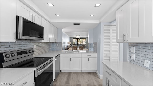 kitchen with tasteful backsplash, white cabinetry, light wood-type flooring, and appliances with stainless steel finishes