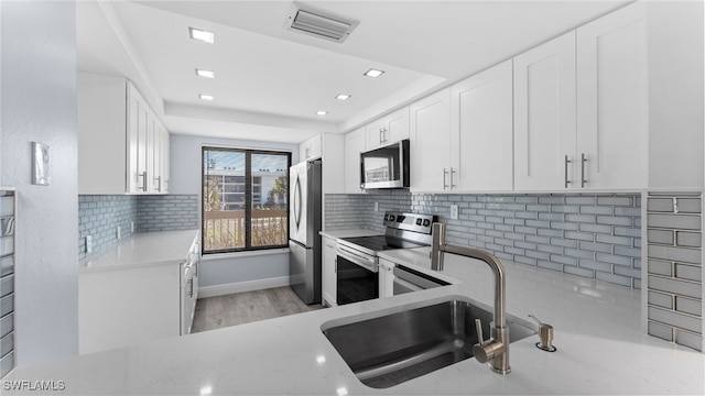 kitchen featuring white cabinets, light wood-type flooring, appliances with stainless steel finishes, and tasteful backsplash