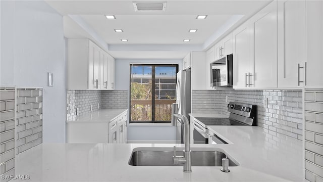 kitchen with tasteful backsplash, sink, white cabinets, and stainless steel appliances