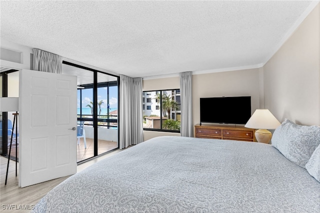 bedroom featuring floor to ceiling windows, access to exterior, light wood-type flooring, and a textured ceiling