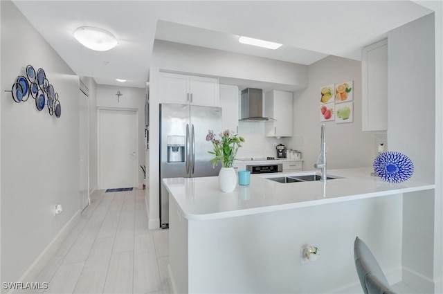 kitchen with wall chimney exhaust hood, kitchen peninsula, stainless steel fridge, white cabinetry, and tasteful backsplash