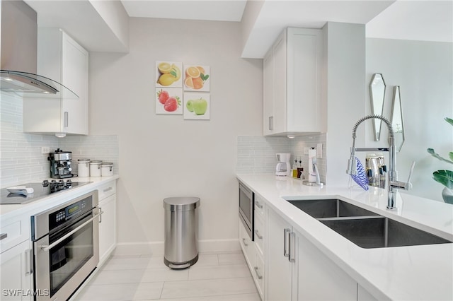 kitchen featuring wall chimney exhaust hood, stainless steel appliances, sink, white cabinetry, and tasteful backsplash