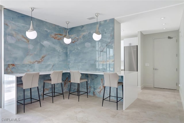 kitchen with kitchen peninsula, a breakfast bar, white cabinetry, stainless steel refrigerator, and decorative light fixtures