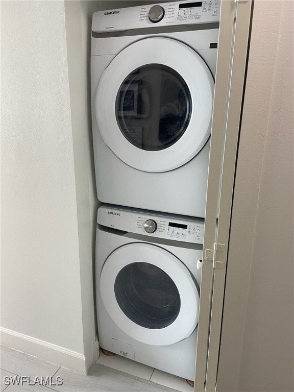 laundry area with stacked washer / drying machine and light tile patterned floors