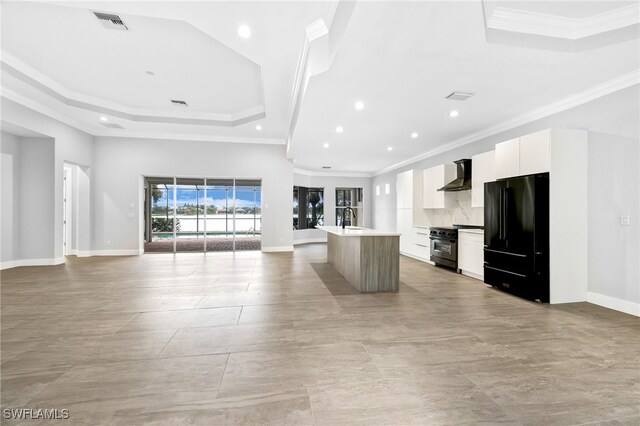 kitchen featuring white cabinetry, black refrigerator, a center island with sink, and wall chimney exhaust hood