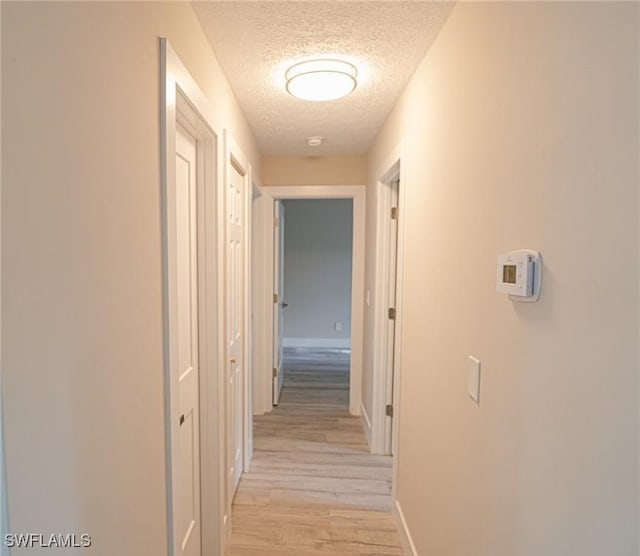 corridor featuring a textured ceiling and light hardwood / wood-style flooring