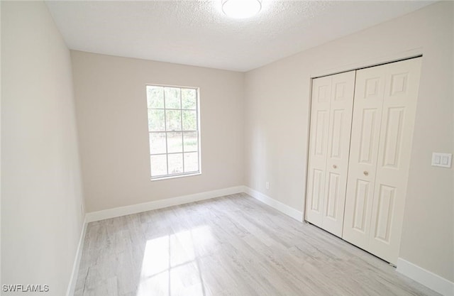 unfurnished bedroom with a textured ceiling, a closet, and light wood-type flooring