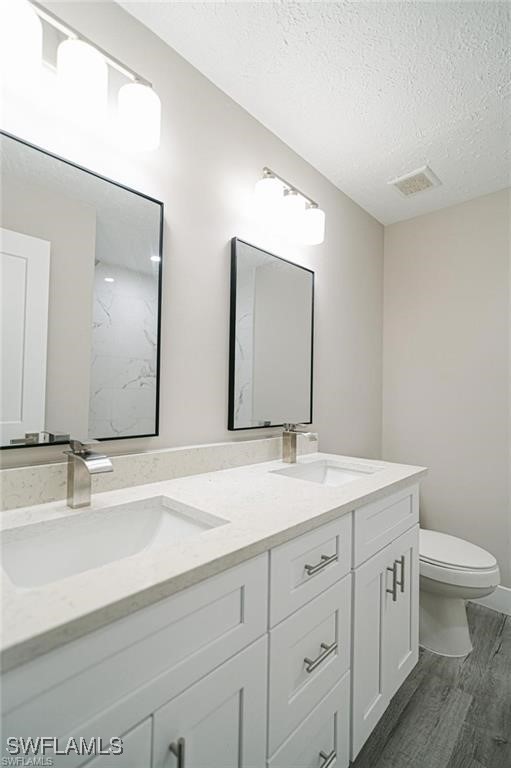 bathroom with a textured ceiling, vanity, toilet, and hardwood / wood-style flooring