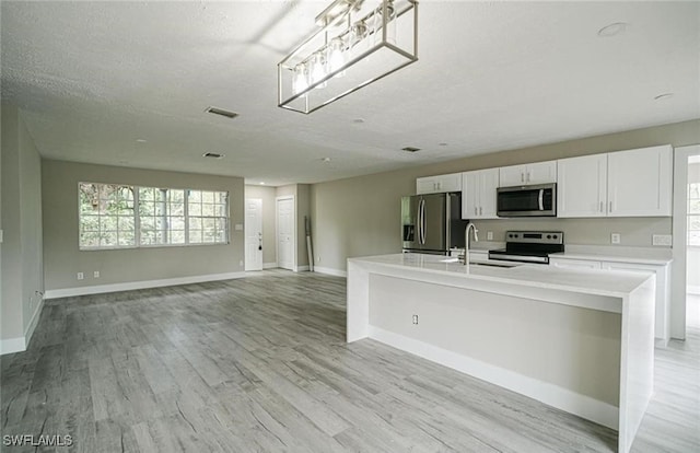 kitchen with a center island with sink, light wood-type flooring, appliances with stainless steel finishes, and white cabinets