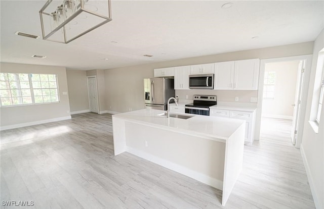 kitchen with a center island with sink, appliances with stainless steel finishes, light hardwood / wood-style floors, sink, and white cabinetry