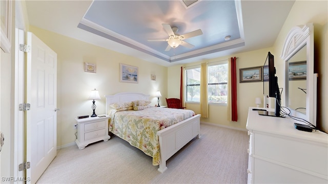 bedroom with baseboards, a raised ceiling, and light carpet