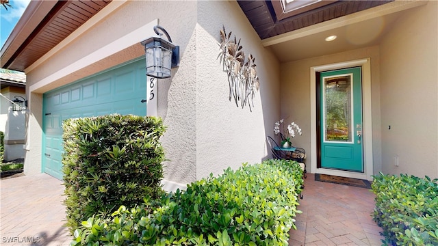 view of exterior entry with an attached garage and stucco siding