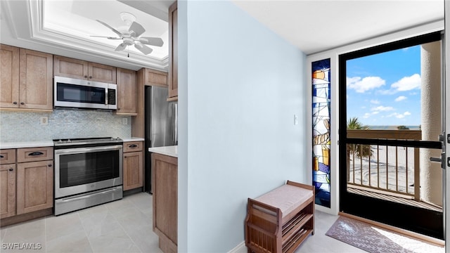 kitchen with appliances with stainless steel finishes, light tile patterned flooring, ornamental molding, ceiling fan, and decorative backsplash