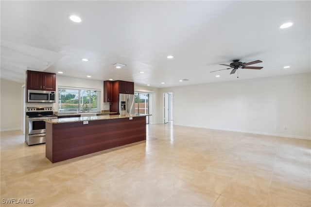 kitchen with light stone countertops, stainless steel appliances, sink, ceiling fan, and a kitchen island