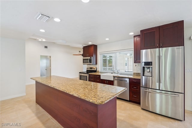 kitchen featuring light stone countertops, a kitchen island, stainless steel appliances, and sink