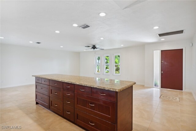 kitchen with light tile patterned floors, light stone counters, a center island, and ceiling fan