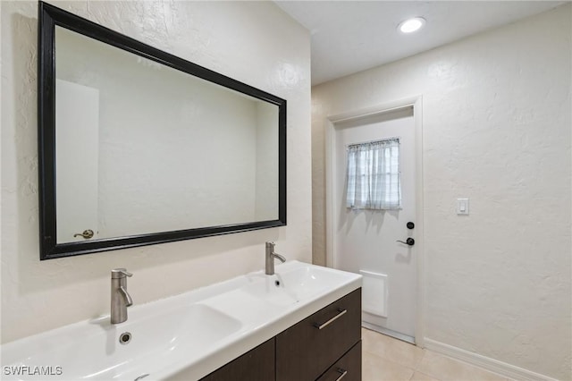 bathroom featuring a sink, a textured wall, double vanity, and tile patterned flooring