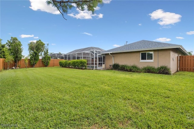 rear view of property with a yard, stucco siding, glass enclosure, and a fenced backyard