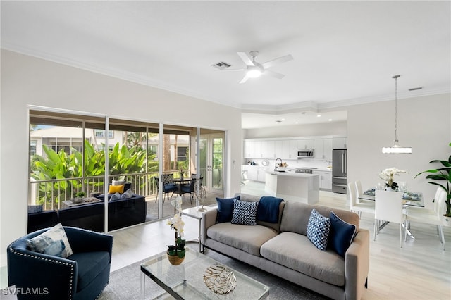 living room featuring ceiling fan, ornamental molding, and light hardwood / wood-style flooring