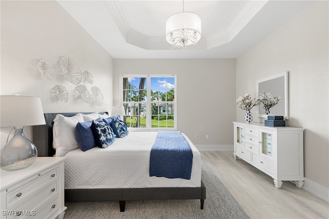 bedroom with an inviting chandelier, light hardwood / wood-style flooring, a tray ceiling, and crown molding