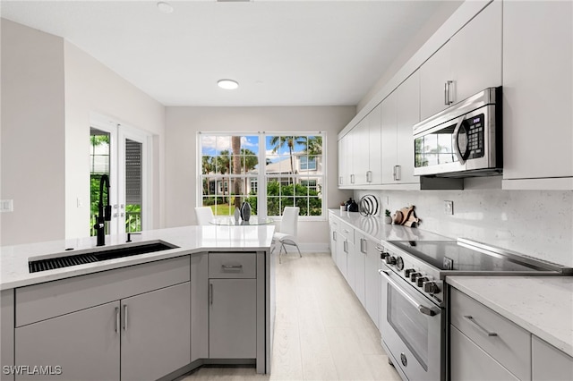 kitchen featuring tasteful backsplash, sink, stainless steel appliances, gray cabinets, and light hardwood / wood-style flooring