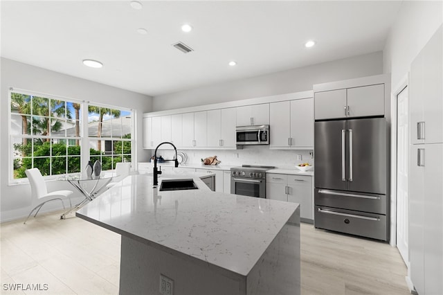 kitchen featuring light stone countertops, appliances with stainless steel finishes, sink, light wood-type flooring, and a kitchen island with sink