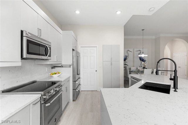 kitchen featuring high quality appliances, sink, pendant lighting, white cabinetry, and light hardwood / wood-style floors