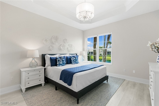 bedroom featuring a chandelier, a tray ceiling, and light hardwood / wood-style floors