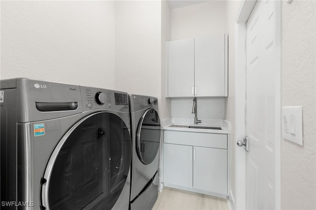 clothes washing area featuring sink, washing machine and dryer, and cabinets